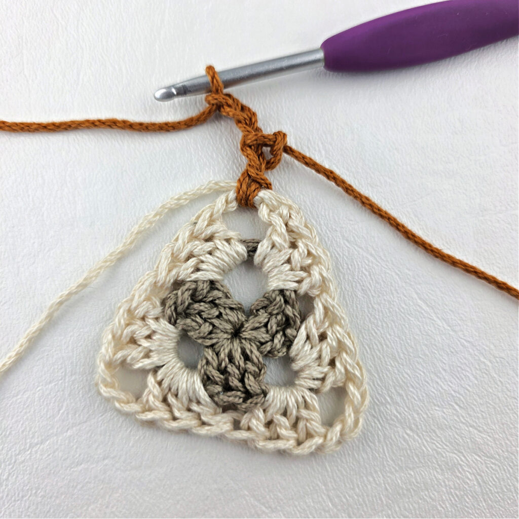 Round 3 of crochet granny stitch triangle with a purple crochet hook.