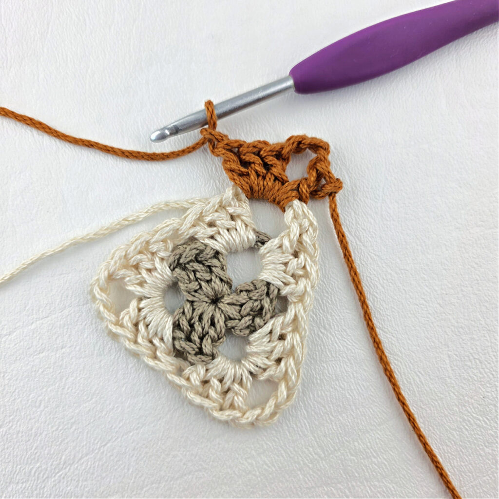 Round 3 of crochet granny stitch triangle with a purple crochet hook.