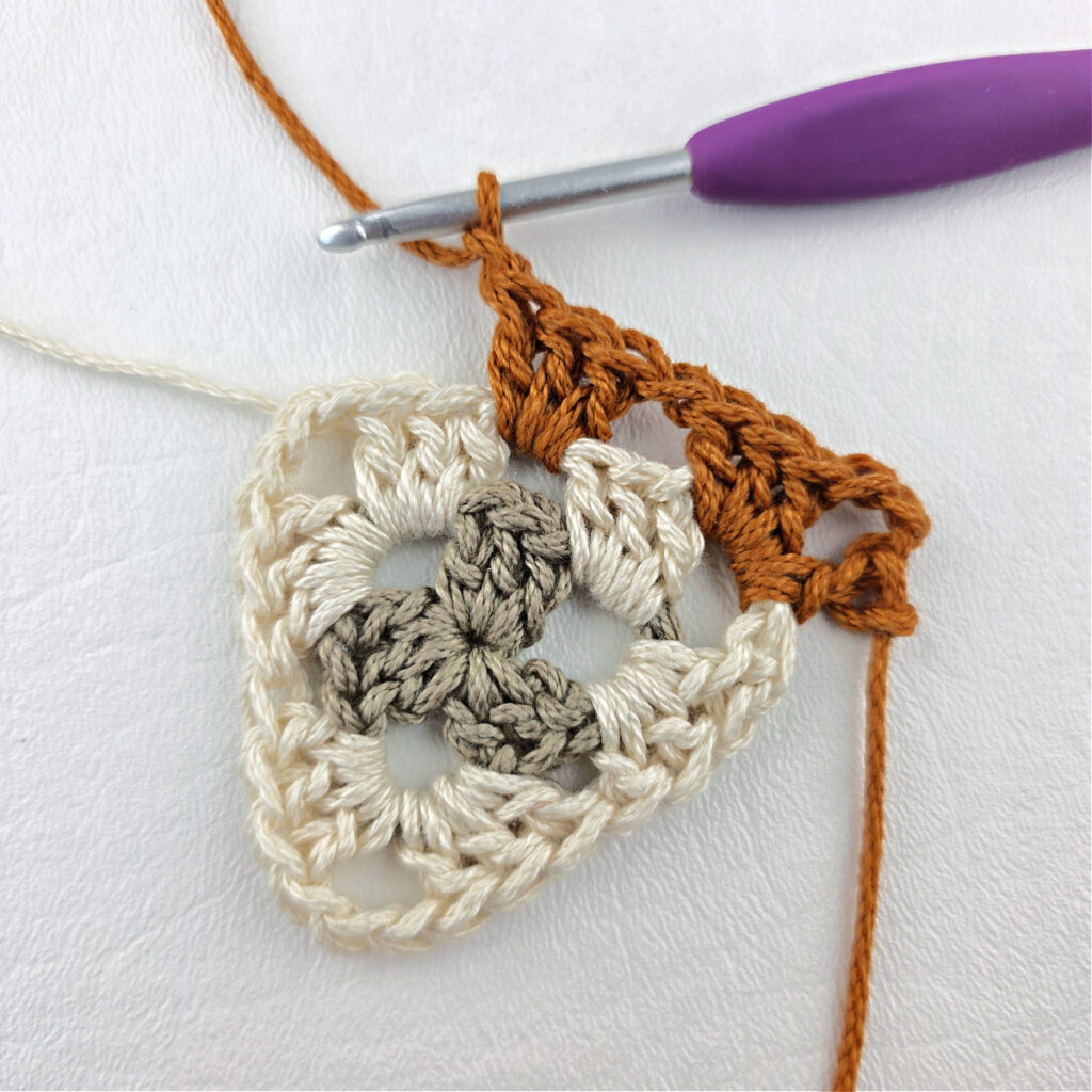 Round 3 of crochet granny stitch triangle with a purple crochet hook.