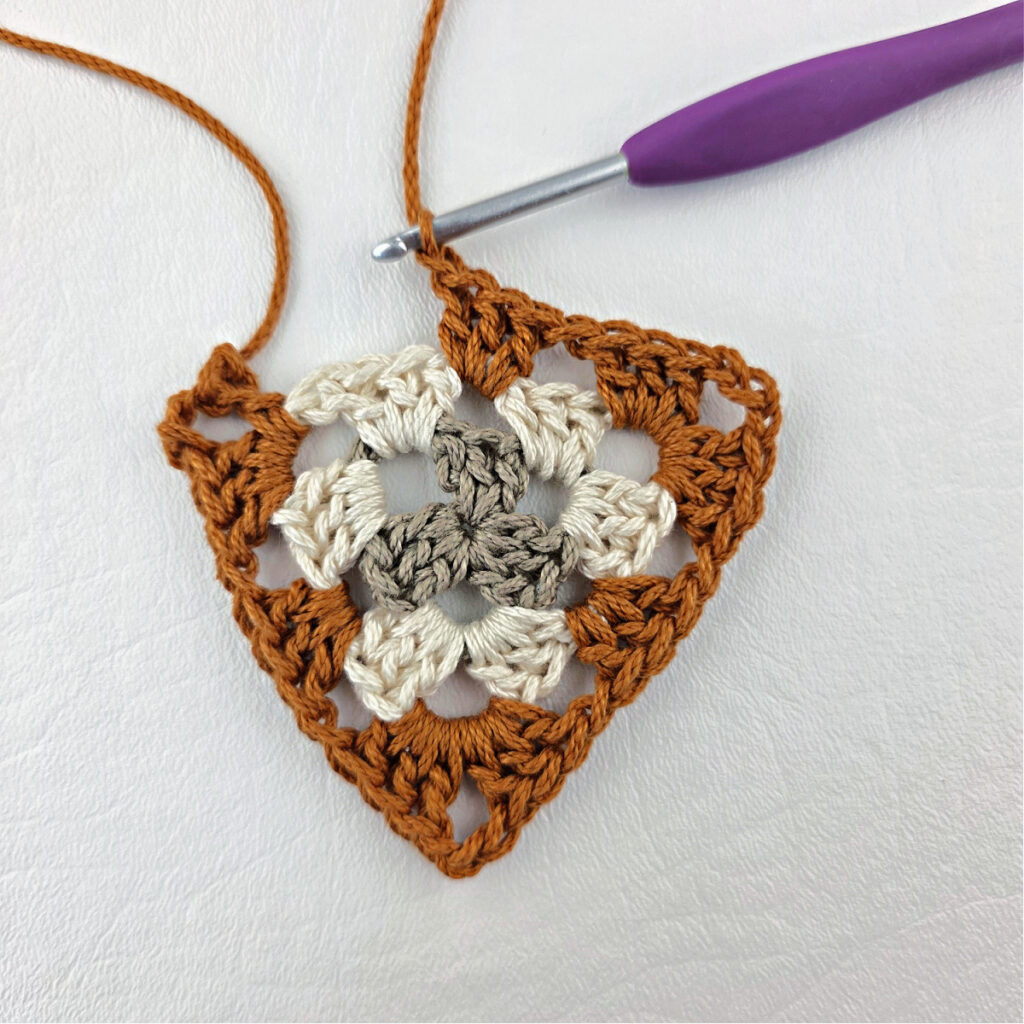 Round 3 of crochet granny stitch triangle with a purple crochet hook.