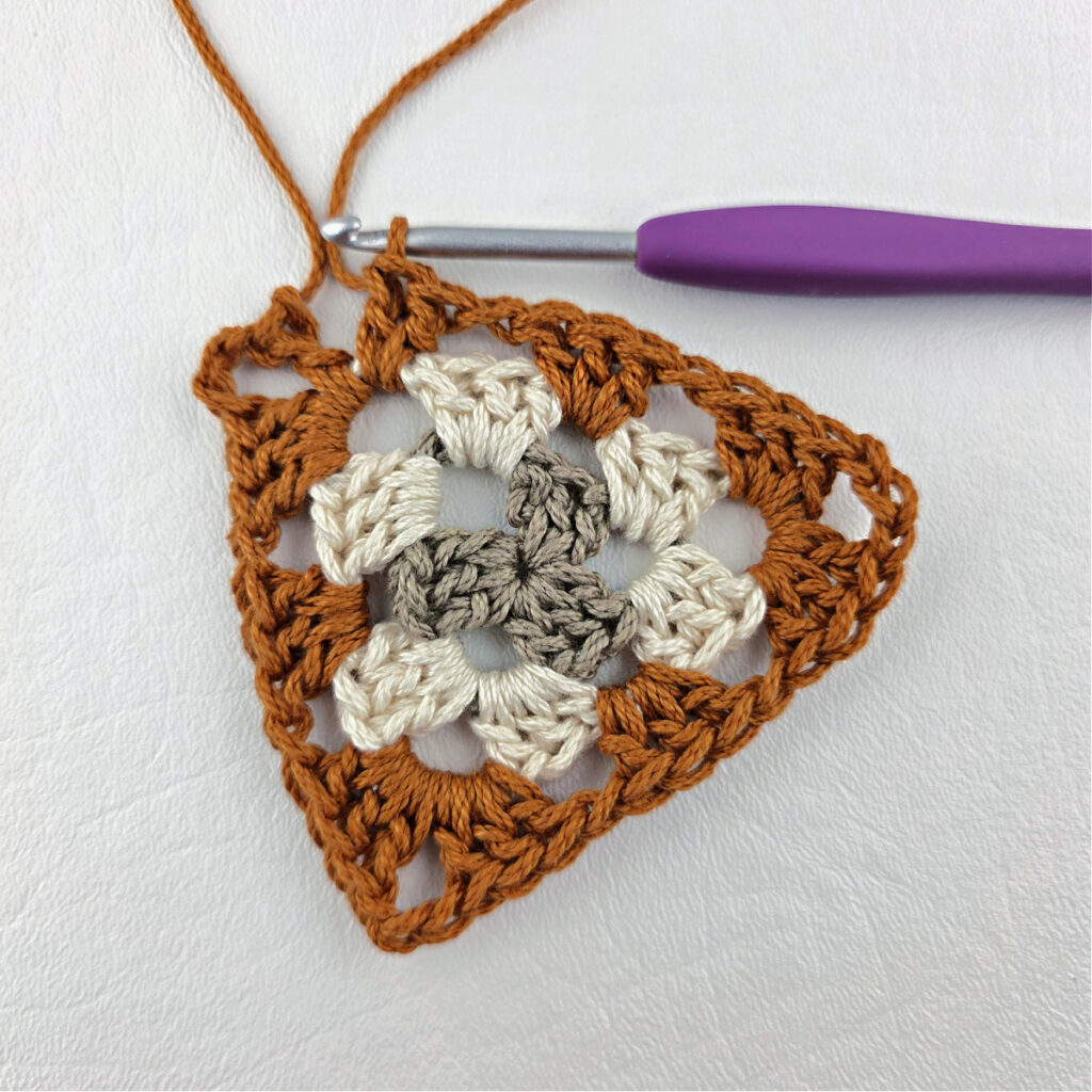 Round 3 of crochet granny stitch triangle with a purple crochet hook.