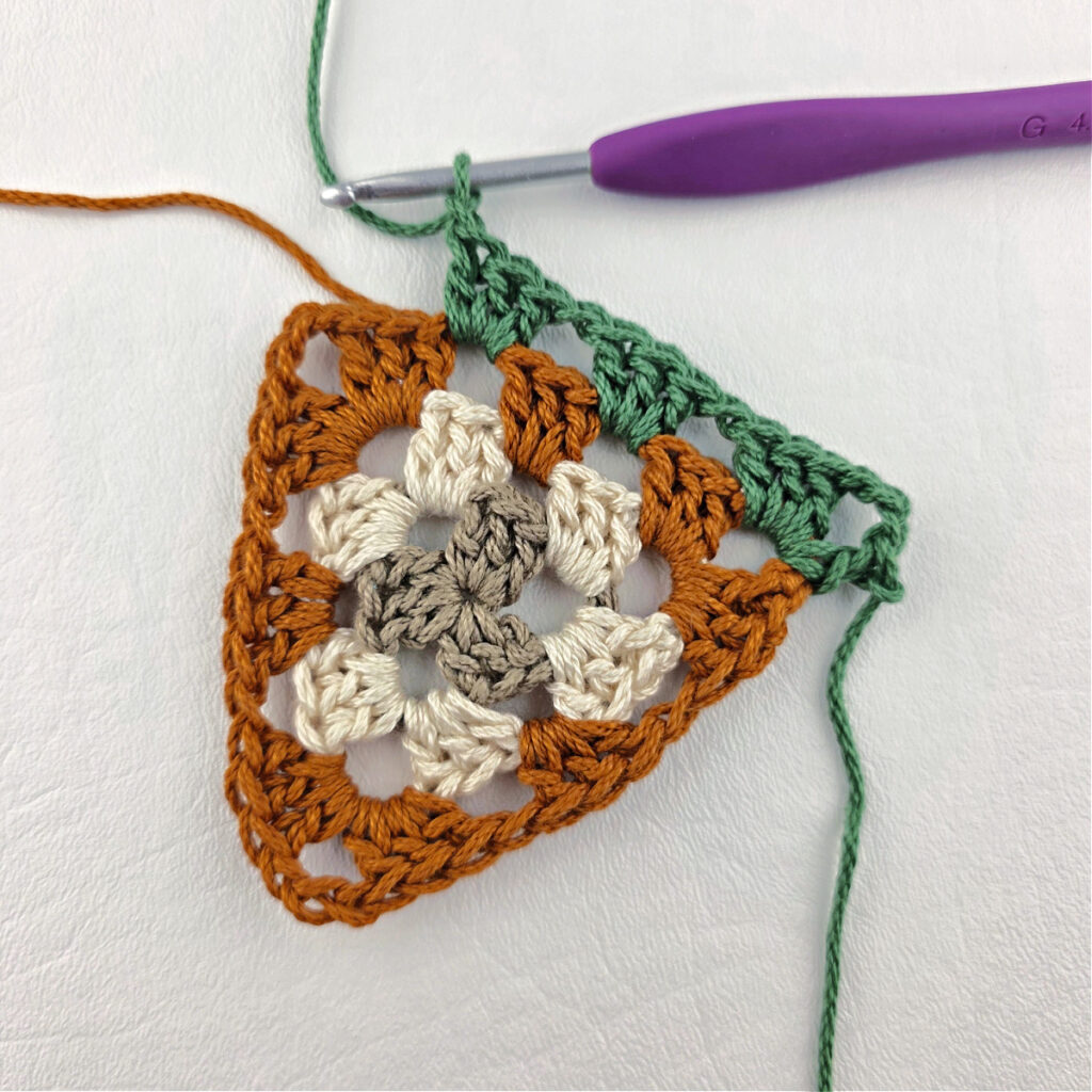 Round 4 of crochet granny stitch triangle with a purple crochet hook.