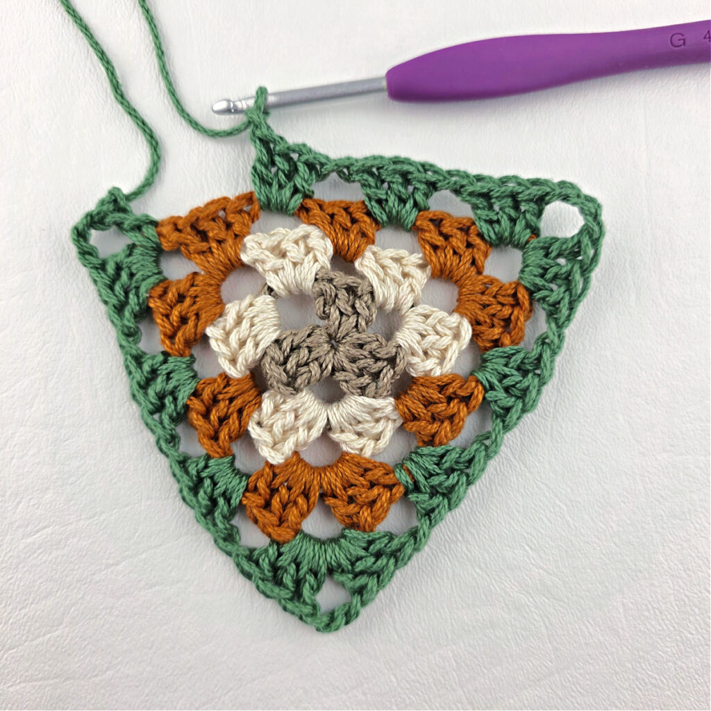 Round 4 of crochet granny stitch triangle with a purple crochet hook.