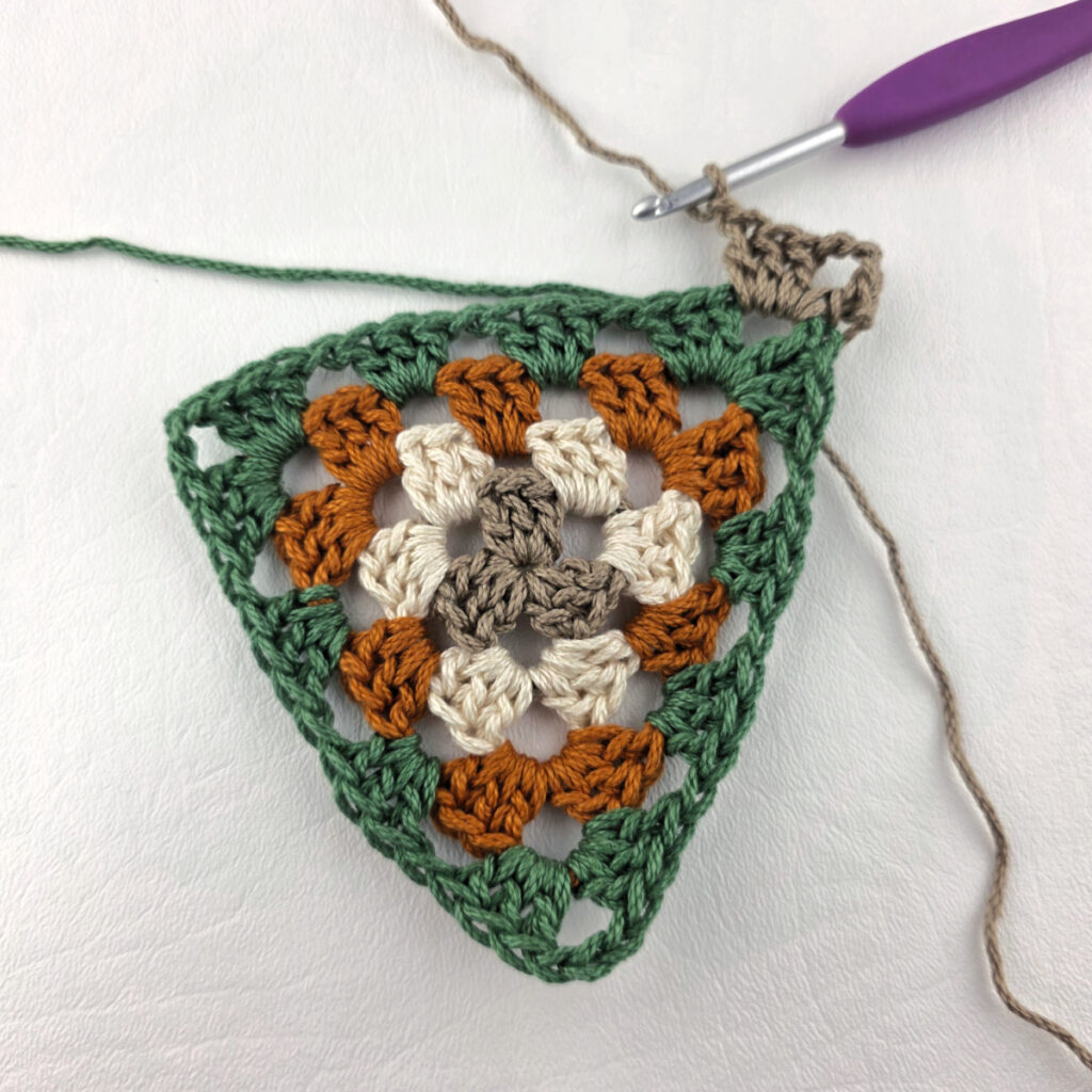 Round 5 of crochet granny stitch triangle with a purple crochet hook.