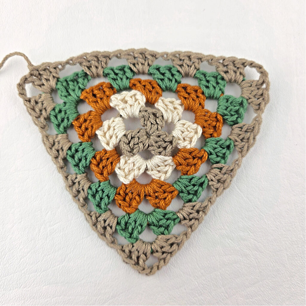 Round 5 of crochet granny stitch triangle with a purple crochet hook.