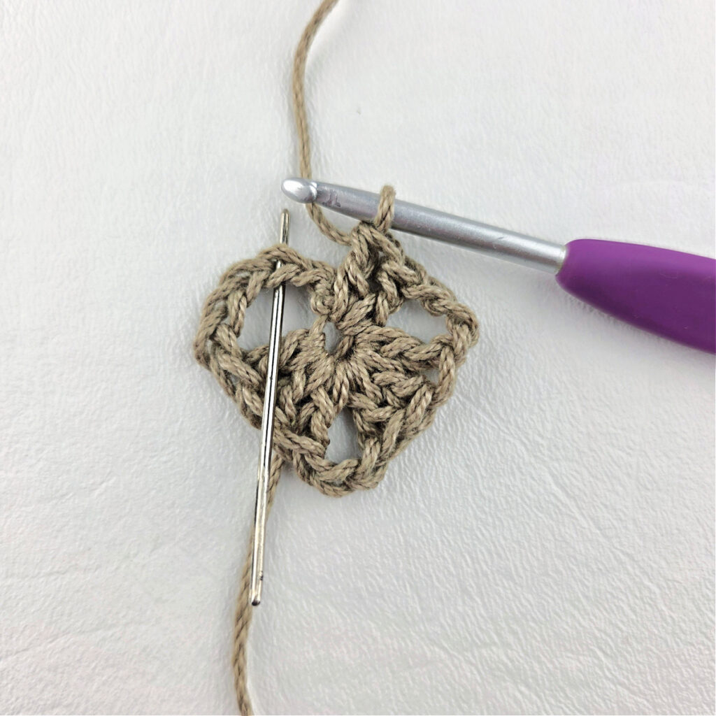 Round 1 of crochet granny stitch triangle with a purple crochet hook.