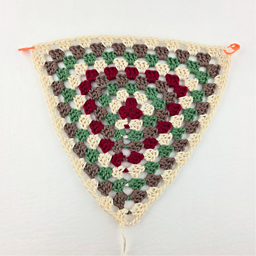 Completed crochet granny stitch triangle with stitch markers in two corners.