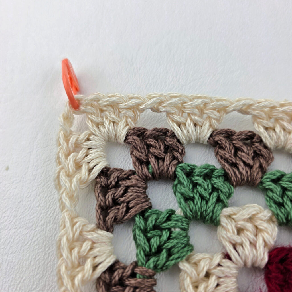 Orange stitch marker in the corner of a granny stitch.