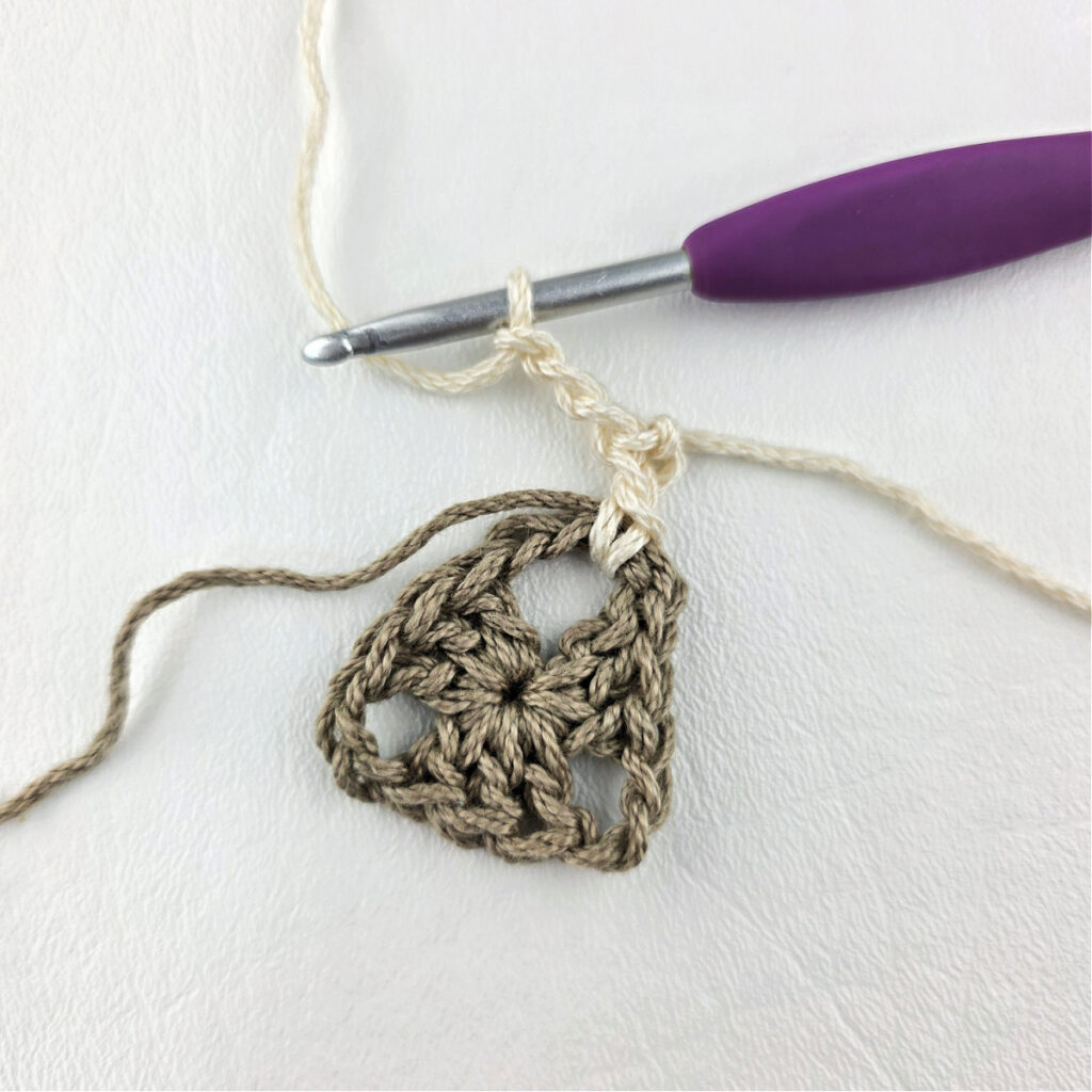 Round 2 of crochet granny stitch triangle with a purple crochet hook.