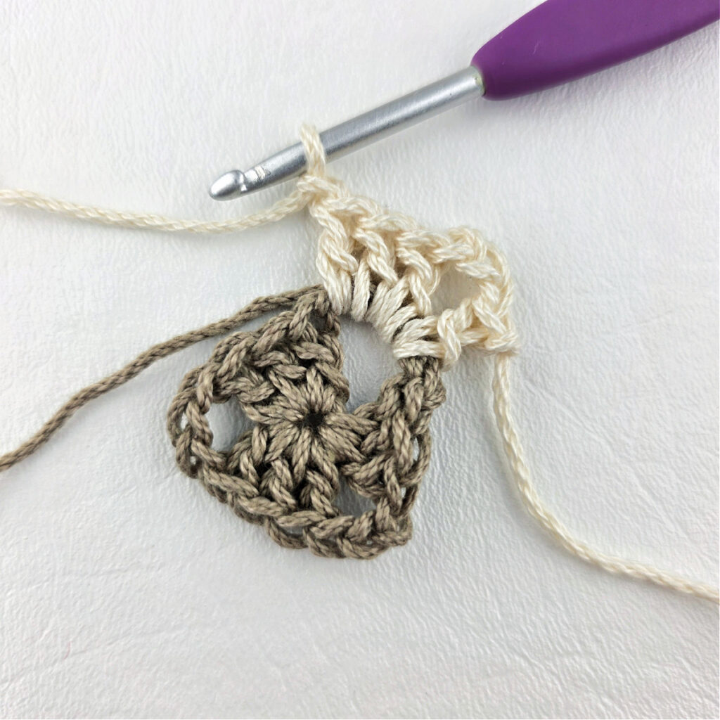 Round 2 of crochet granny stitch triangle with a purple crochet hook.