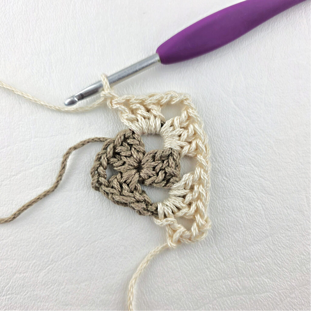 Round 2 of crochet granny stitch triangle with a purple crochet hook.