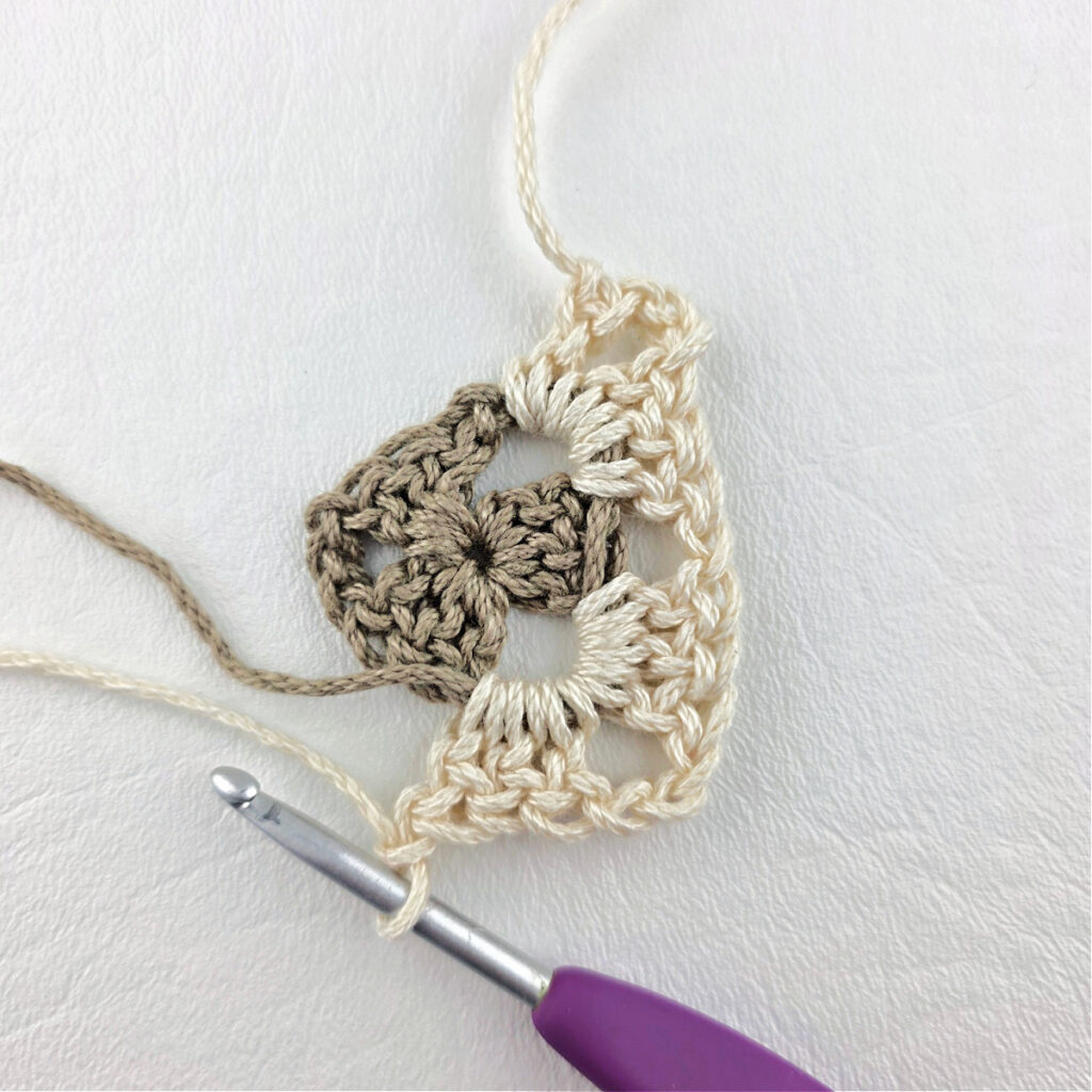 Round 2 of crochet granny stitch triangle with a purple crochet hook.