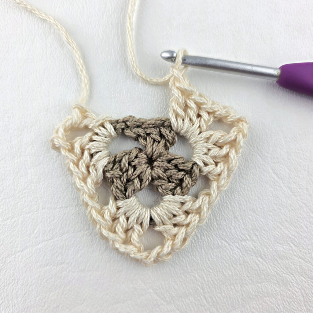 Round 2 of crochet granny stitch triangle with a purple crochet hook.