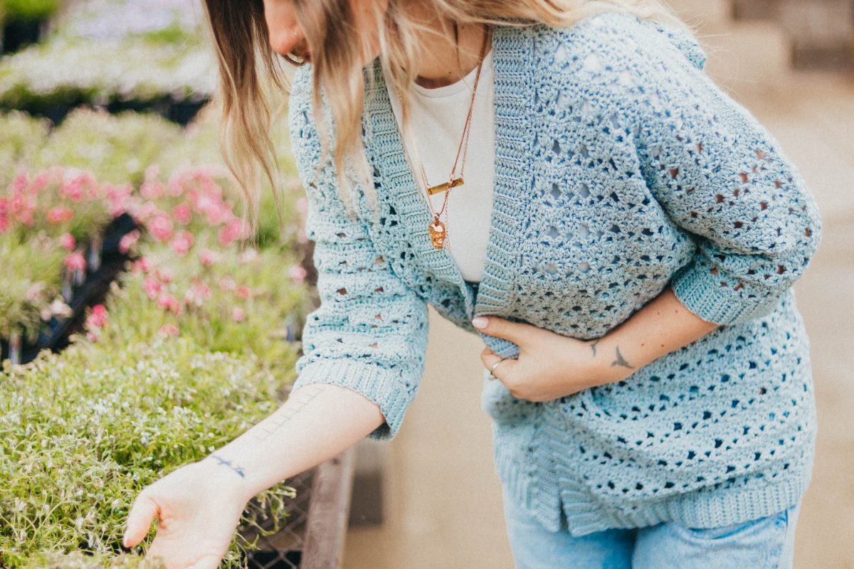 Girl wearing a light blue summer crochet cardigan bending to see plants.