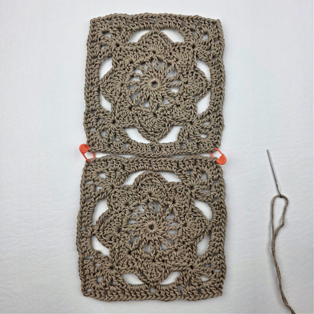 Joining two crochet granny squares together with a stitch marker and needle.