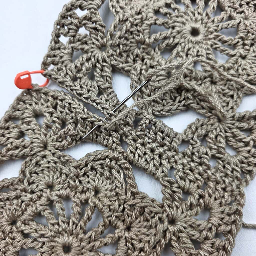Joining crochet granny squares together with a stitch marker and needle.