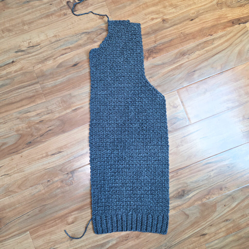Working a blue grey colored crochet mens cardigan against a wooden background.
