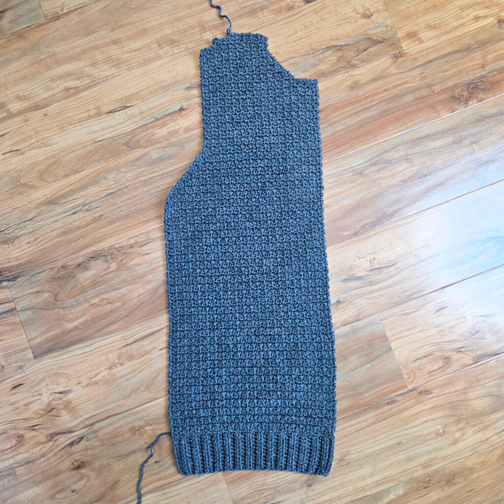 Working a blue grey colored crochet mens cardigan against a wooden background.