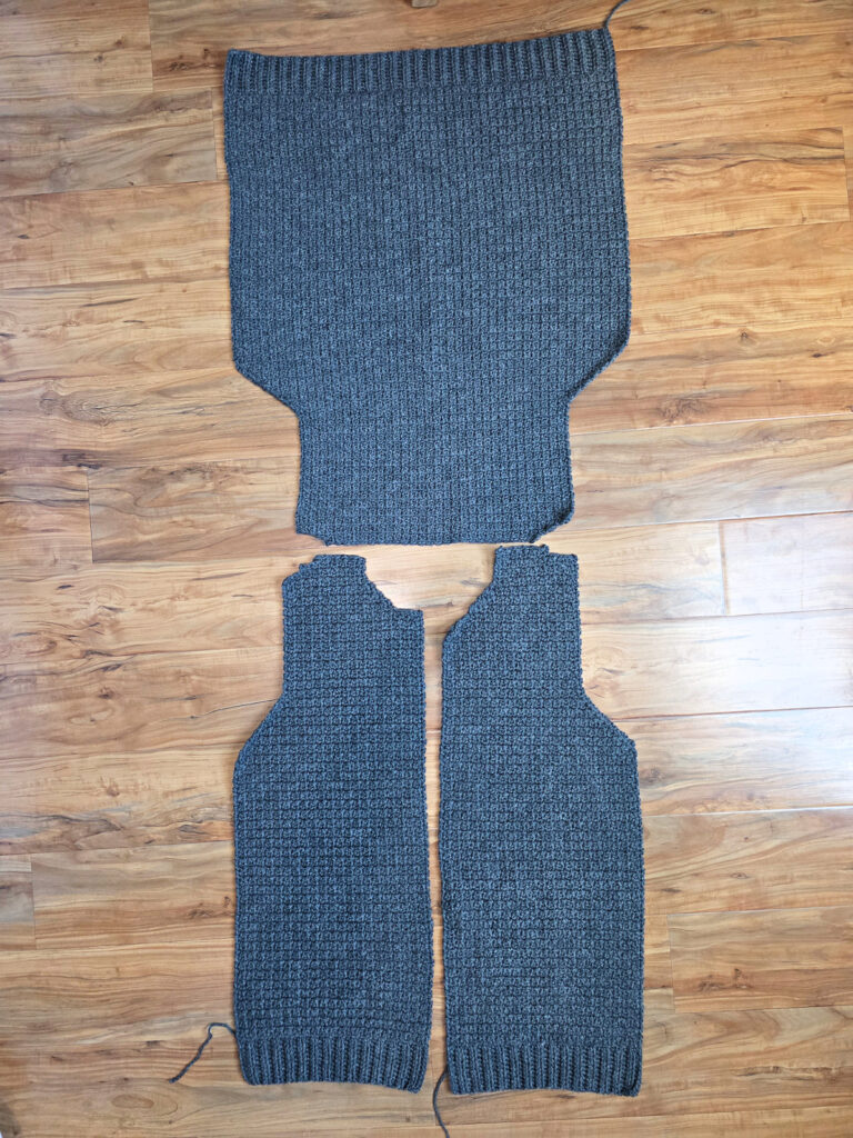 Working a blue grey colored crochet mens cardigan against a wooden background.