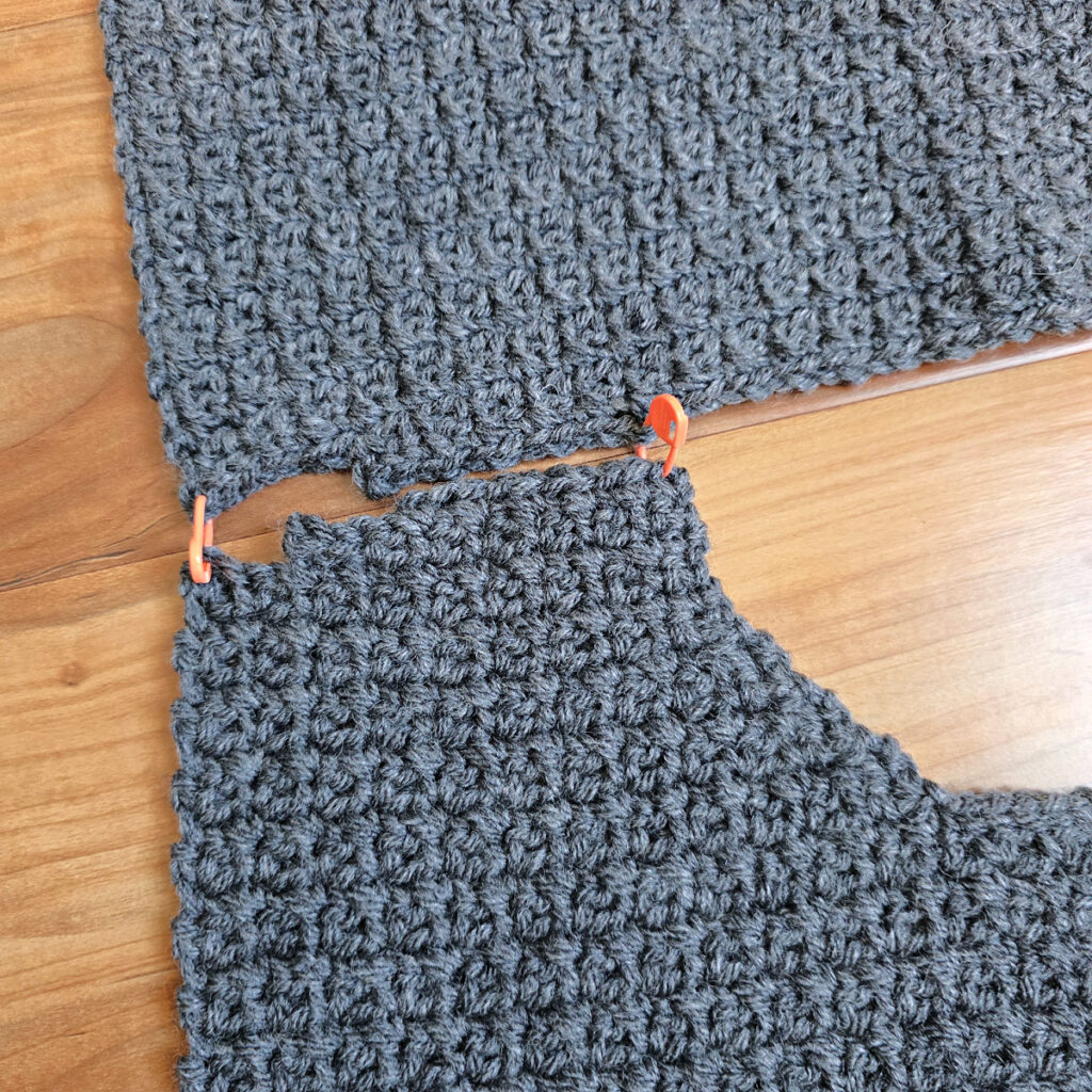 Working a blue grey colored crochet mens cardigan against a wooden background.