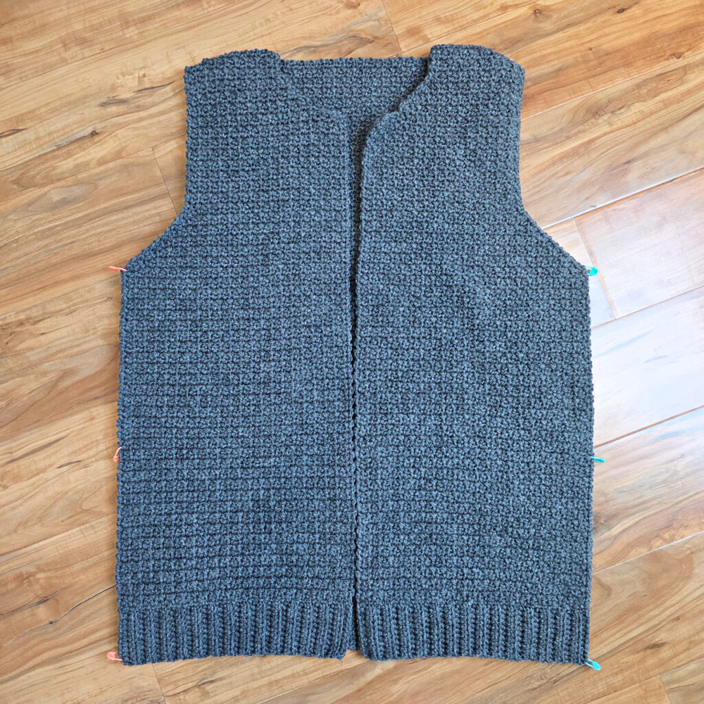 Working a blue grey colored crochet mens cardigan against a wooden background.