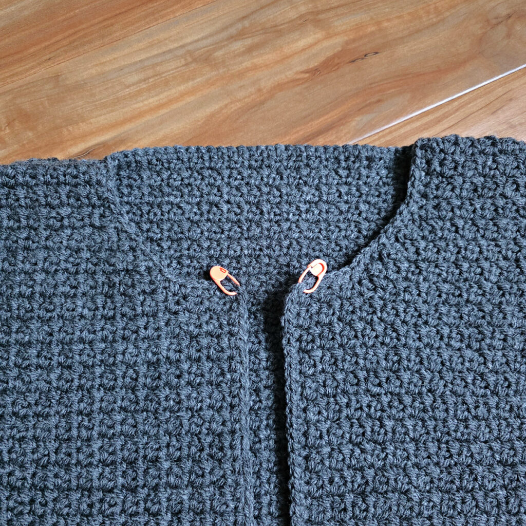 Working a blue grey colored crochet mens cardigan against a wooden background.